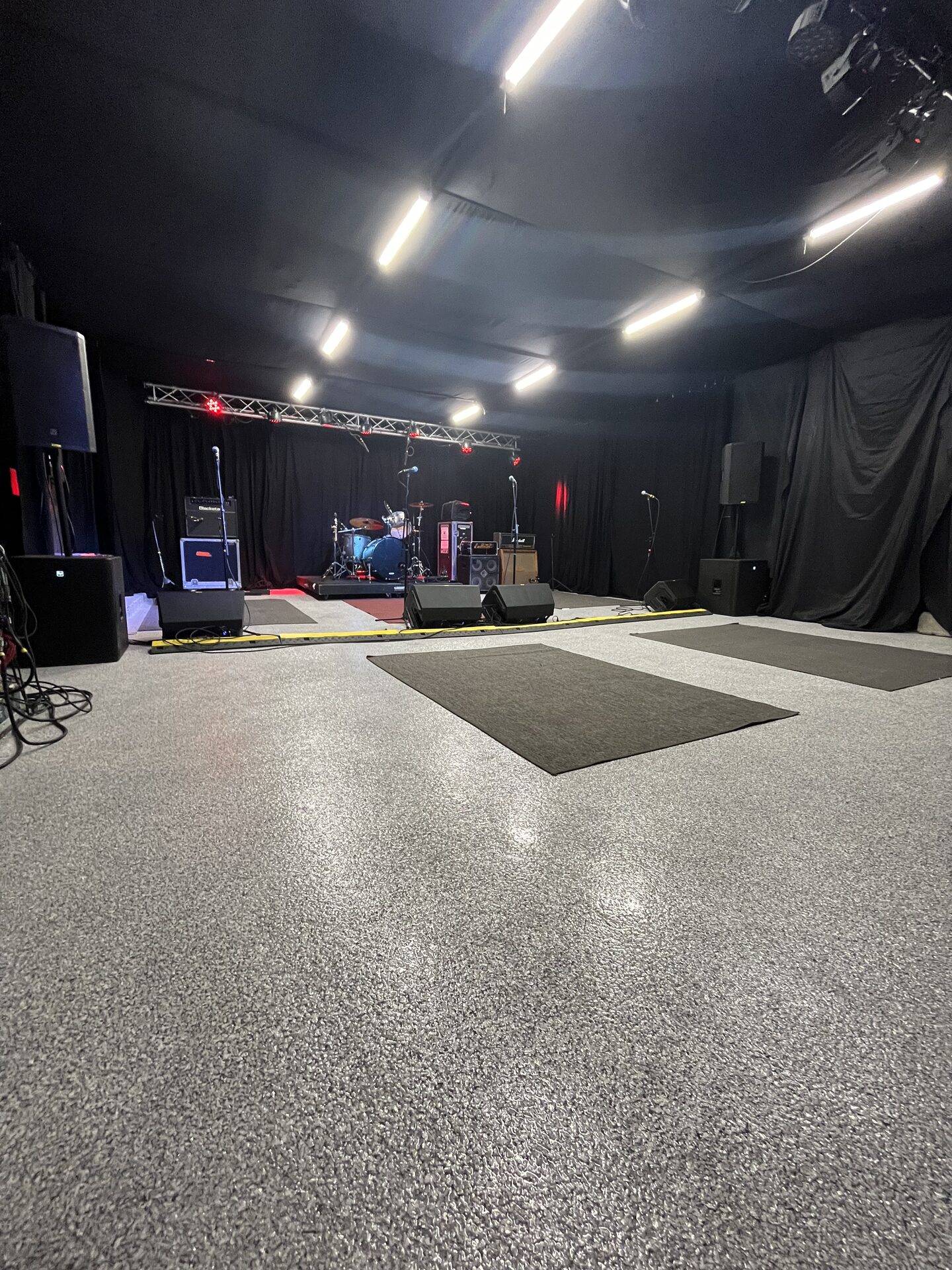 Rock Mill rehearsal room configured with full drum kit, PA stack, and stage lighting